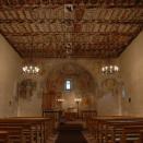 The nave of the old church of San Gian in Celerina Switzerland. Hanging iron chandeliers, painted flat ceiling and frescoes on the walls.